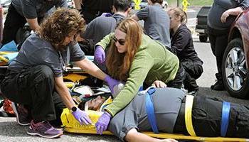 两名学生对躺在板上的学生病人练习急救技能. 高级急救医疗技术员证书